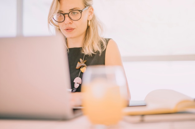 Defocused glass of juice in front of businesswoman using laptop