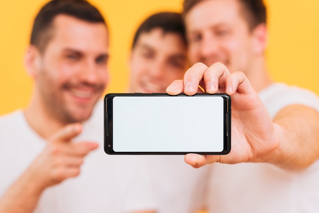 Defocused three male friend showing smart phone with white screen