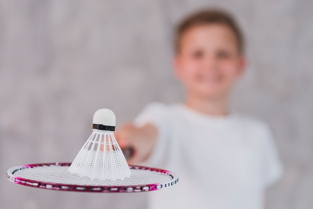 Free Photo defocussed boy holding shuttlecock on racket against grey wall