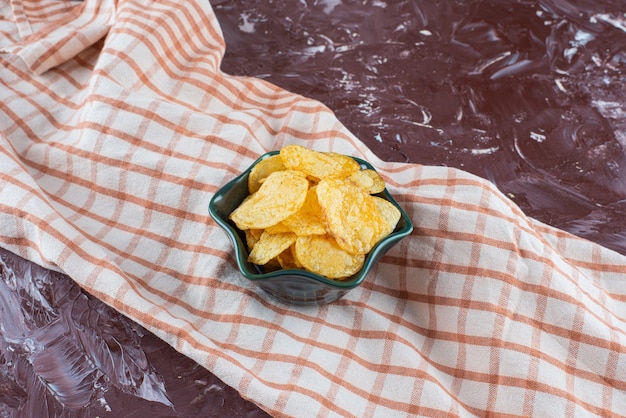 Free photo delectable potato chips in a bowl on tea towel , on the marble table.