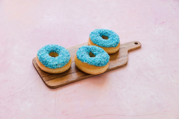 Delicious blue donuts on wooden chopping board