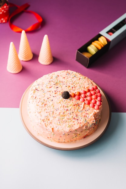 Delicious cake with waffles cones and macaroons on pink and white background