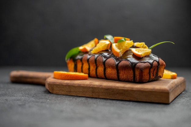 Delicious cakes decorated with orange and chocolate on wooden cutting board on black table