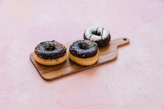 Delicious chocolate donuts on wooden chopping board