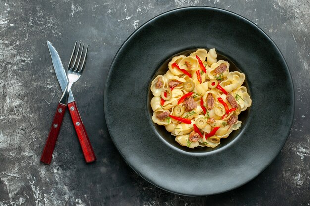 Delicious conchiglie with vegetables greens on a plate and knife on gray table