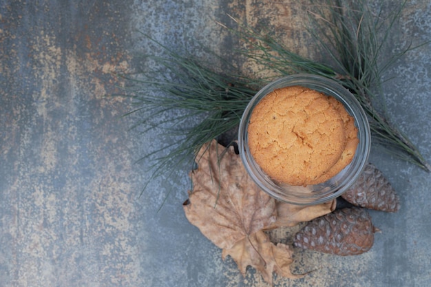 Free Photo delicious cookies in glass jar with leaves and pinecones on marble table.