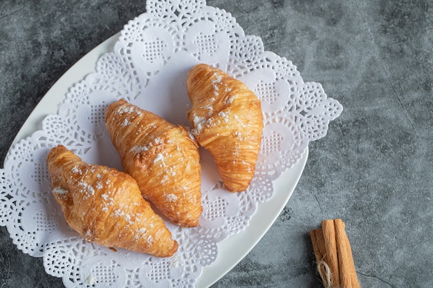 Free photo delicious croissants with cinnamon sticks on gray.