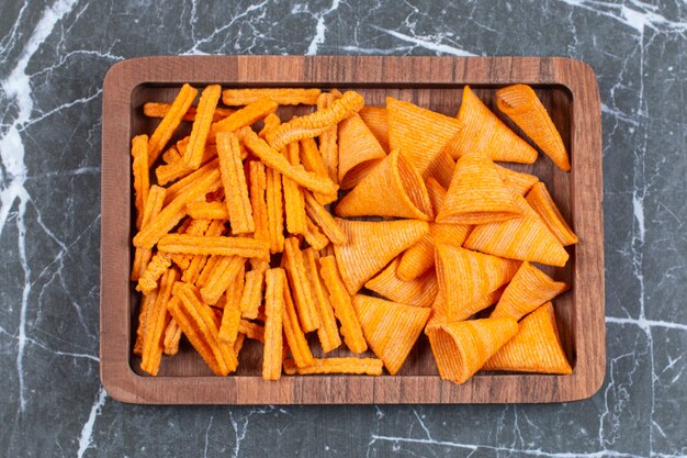 Delicious crunchy stick and triangle chips on wooden plate.