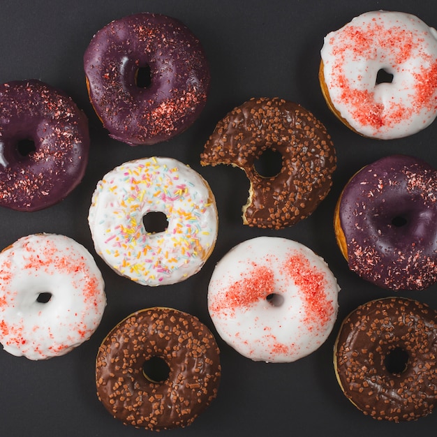 Free photo delicious different bitten doughnuts with icing on black background