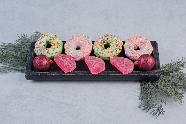 Delicious donuts with sprinklers and marmalades on black plate. 