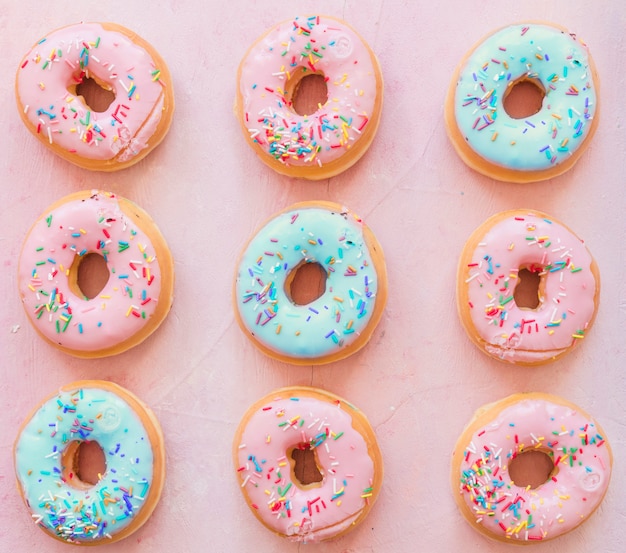 Delicious donuts with sprinkles on pink background