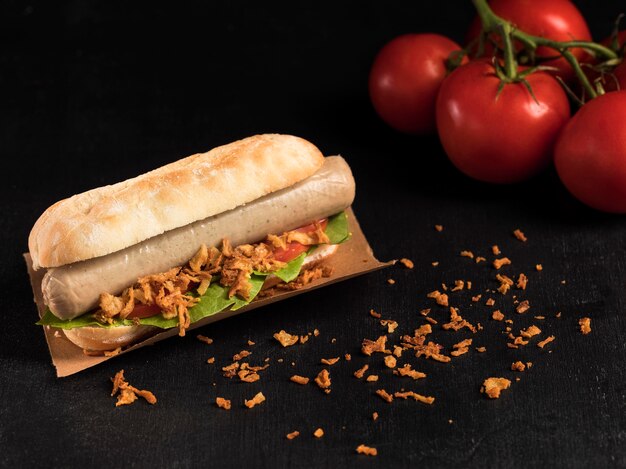 Delicious fast-food hot dog on baking paper and tomatoes