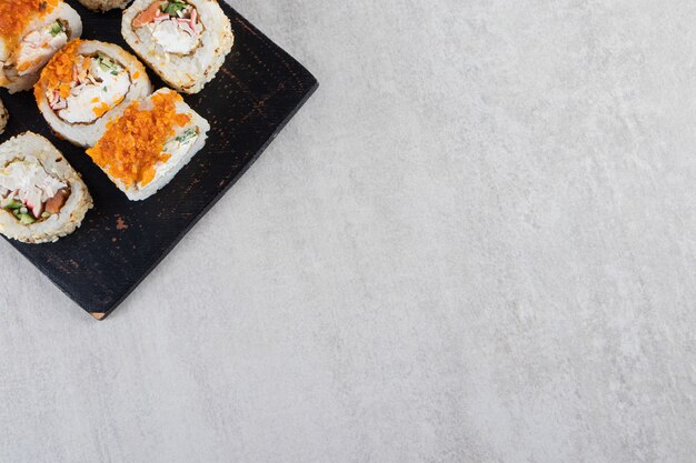 Delicious fresh sushi rolls placed on a dark wooden board . 