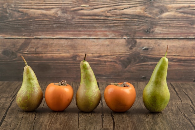 Free Photo delicious fuyu persimmons and ripe pears on wooden surface