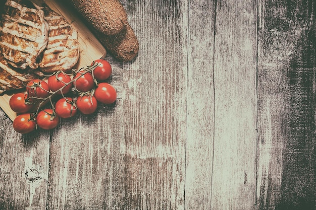 Free photo delicious grilled chicken on wooden board next to healthy bread, tomatoes and salad. healthy lifestyle and eating