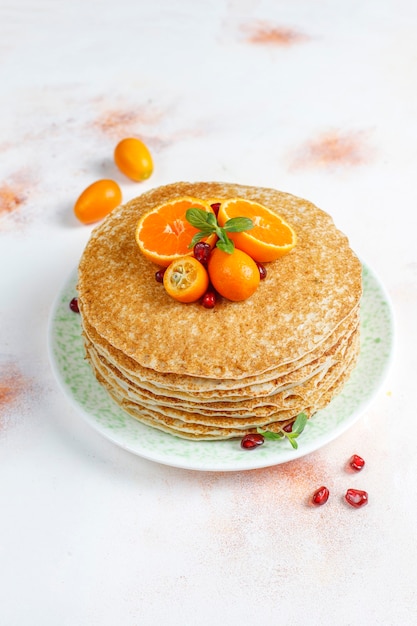 Free photo delicious homemade crepe cake decorated with pomegranate seeds and mandarins.