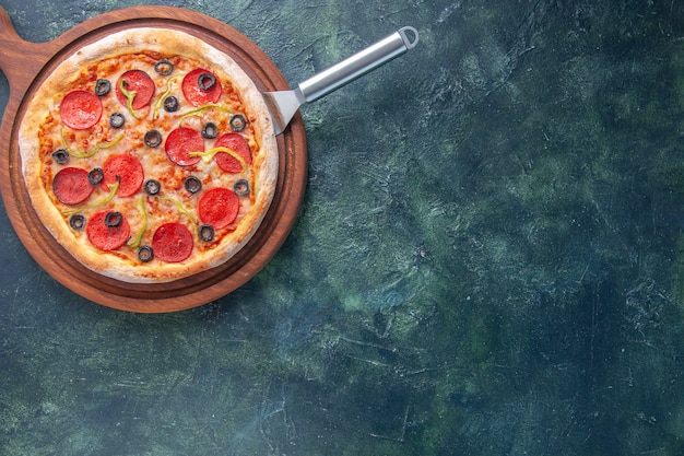 Delicious homemade pizza on cuttingwooden board on the right side on dark surface