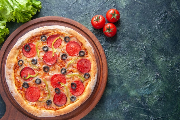 Delicious homemade pizza on wooden cutting board tomatoes ketchup green bundle on dark surface