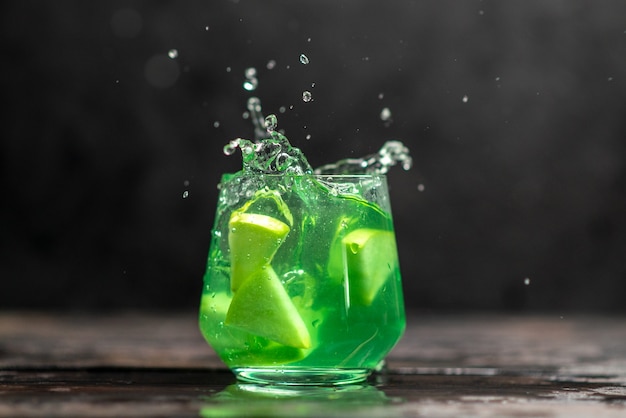 Free Photo delicious juice in a glass with apple limes on dark background