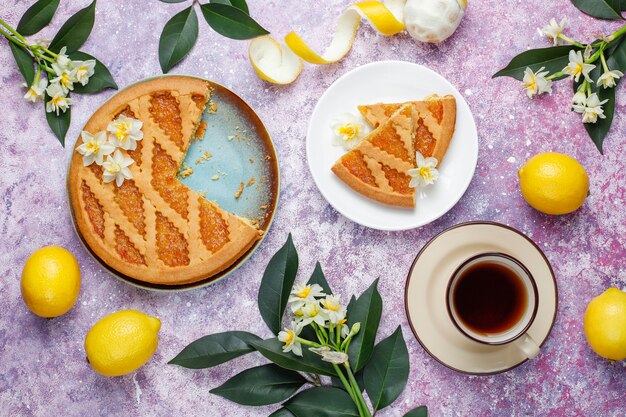 Delicious lemon pie slices with fresh lemons and a cup of tea ,top view