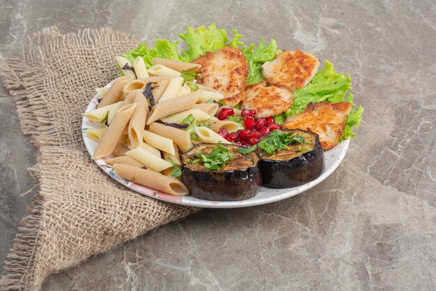 Delicious macaroni with pomegranate and lettuce on white plate.