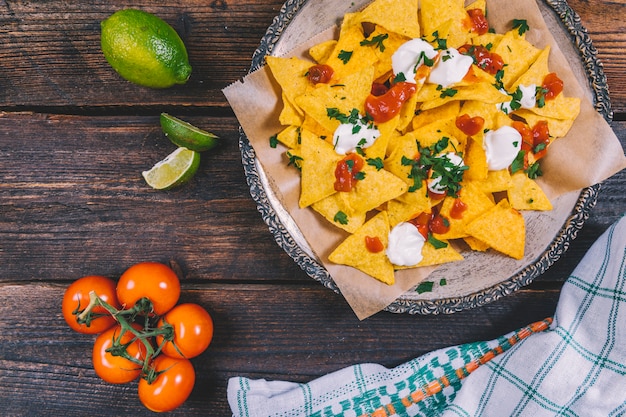 Delicious mexican nachos in plate; lemon slices; cherry tomatoes and cloth on table