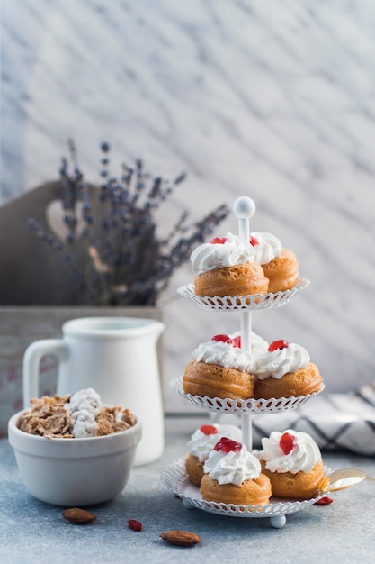 Free photo delicious muffins on cake stand near bowl of cornflakes and almond on concrete surface