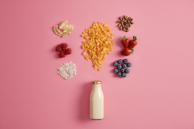 Free photo delicious nourishing breakfast. bottle of milk or yoghurt with granola and tasty ingredients to add. dried apple, raspberry, coconut flakes, pistachio, strawberry, blueberry for preparing tasty meal