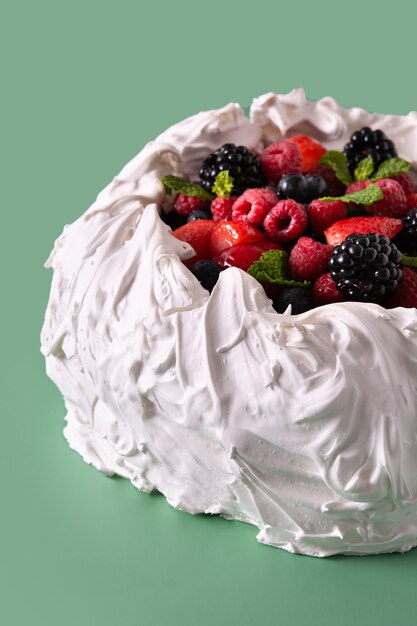 Delicious Pavlova cake with meringue topped and fresh berries on green background