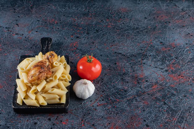 Delicious penne pasta and chicken leg on black cutting board. 