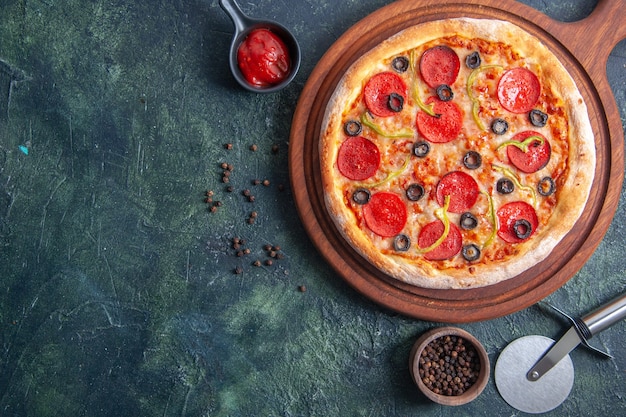 Delicious pizza on wooden cutting board and pepper ketchup on isolated dark surface in close up shot