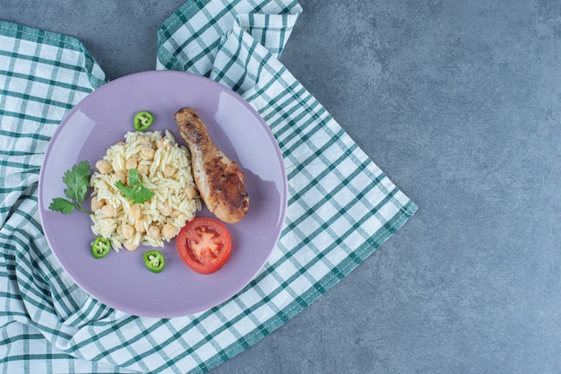 Delicious rice with chickpeas and drumstick on purple plate. 