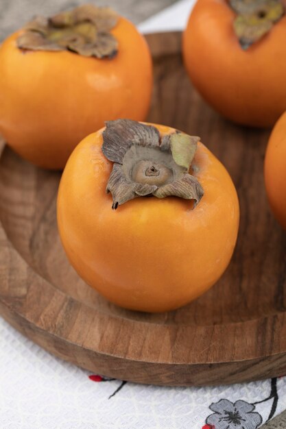 Delicious ripe persimmon fruits placed on wooden plate