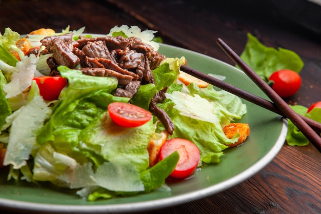 Free photo delicious salad meal in a plate with chopsticks on a wooden background high angle view