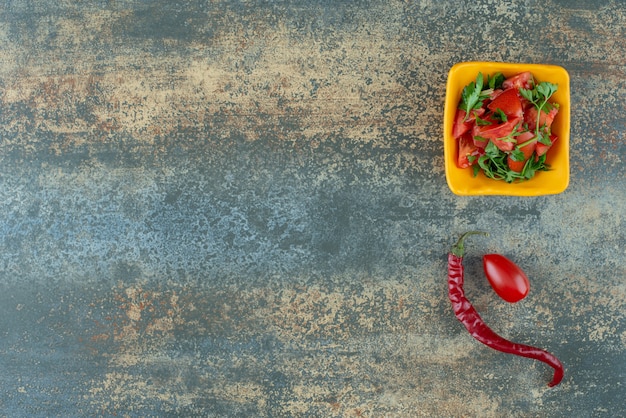 Delicious salad in yellow plate with pepper and tomato on marble background