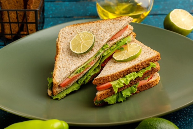 delicious sandwich with green salad tomatoes and ham inside plate on blue