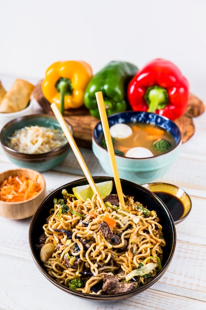 Free Photo delicious stir fry noodles with beef on chopsticks with soup bowl over the wooden desk