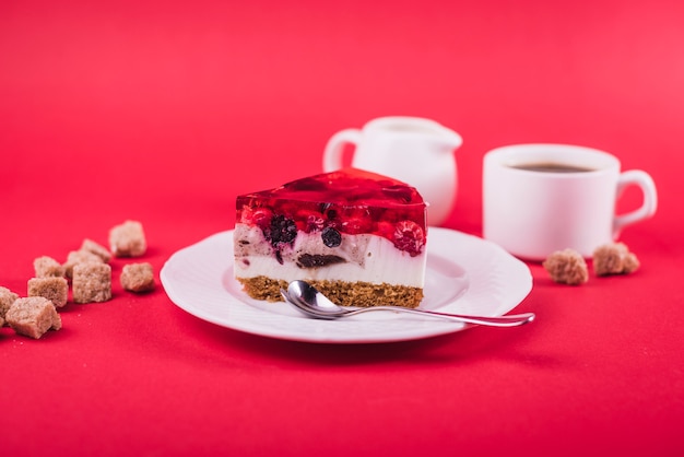 Free Photo delicious strawberry jelly and cheese cake on white plate with brown sugar cubes against red backdrop