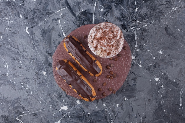 Delicious sweet chocolate eclairs and cup of coffee on wood piece.