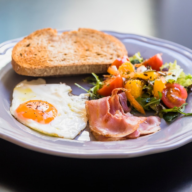 Free photo delicious toast; half fried egg; bacon and salad on gray plate