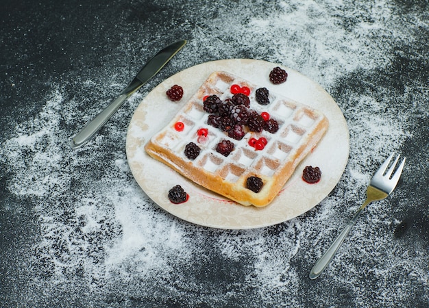 Free photo delicious waffle in a plate with blackberries, fork high angle view on dark