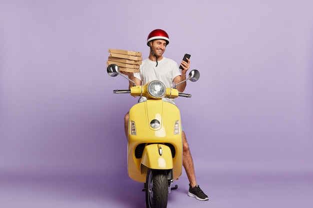 Free photo delighted deliveryman driving scooter while holding pizza boxes