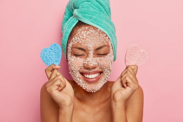 Free Photo delighted healthy woman laughs sincerely, keeps eyes closed, shows white perfect teeth, has overjoyed face expression, applies scrub mask for reducing pimples and refreshing