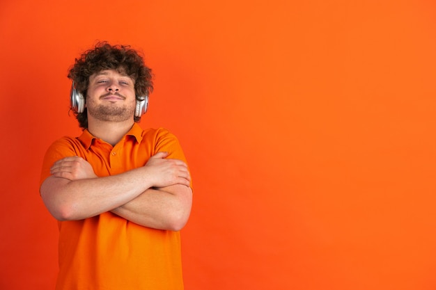 Free Photo delighted listen to music. caucasian young man's monochrome portrait on orange  wall. beautiful male curly model in casual style. concept of human emotions, facial expression,.