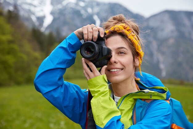 Delighted young European woman takes photo during hiking trip, holds professional camera