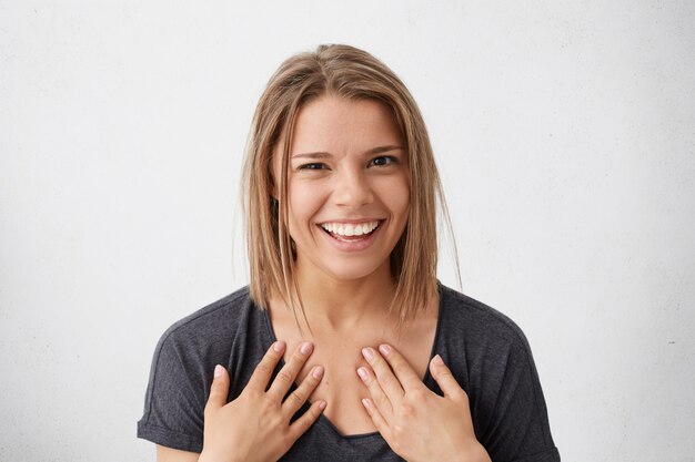 Delightful cute woman with trendy hairstyle and shining brown eyes smiling broadly pointing at herself being proud of her success and victory. Woman smiling broadly having pleasant expression