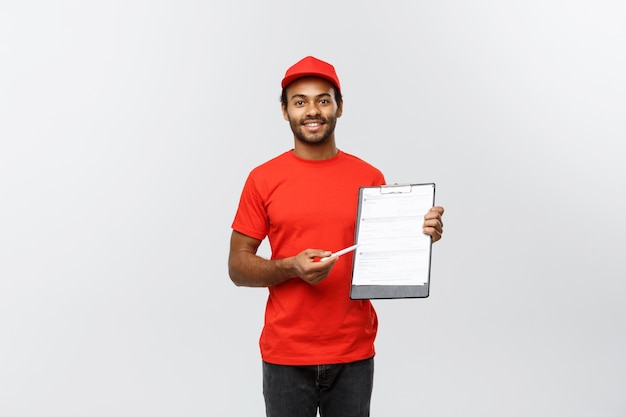 Free Photo delivery concept - portrait of handsome african american delivery man or courier showing a confirmation document form to sign. isolated on grey studio background. copy space.