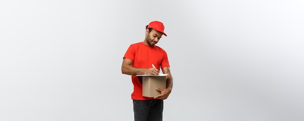 Free Photo delivery concept portrait of handsome african american delivery man or courier writing on a order document isolated on grey studio background copy space