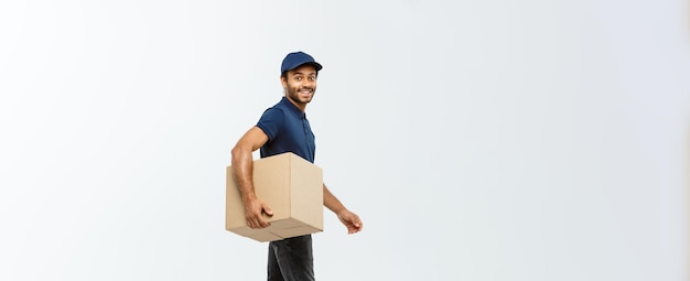 Delivery Concept Portrait of Happy African American delivery man in blue cloth walking to send a box package to customer Isolated on Grey studio Background Copy Space