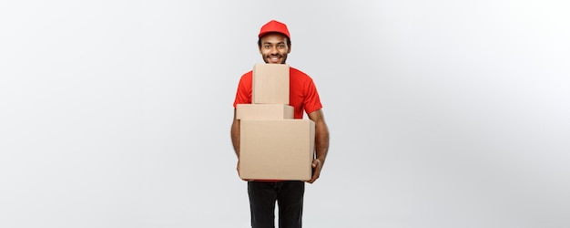 Delivery Concept Portrait of Happy African American delivery man in red cloth holding a box package Isolated on Grey studio Background Copy Space